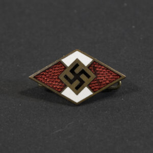 Overview photo of a WWII Hitler Youth membership pin, showing the small diamond‑shaped badge with its red‑white‑black enamel design. The pin is displayed from the front with its metal fastening visible behind it.