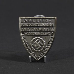 Overview photo of a WWII German DAF “Arbeitsbeschaffung” tinnie, showing the full badge with its circular shape, raised relief design, and metal finish. The front inscription and emblem are visible, along with the overall condition of the piece.