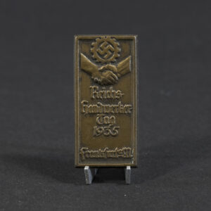 Overview photo of a 1935 “Reichshandwerkertag Frankfurt a. M.” tinnie, showing the full badge with its rectangular shape, raised relief design, and metal finish. The event title and central emblem are visible, along with the overall condition of the piece.