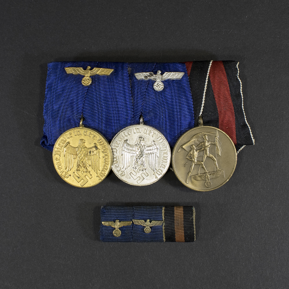 Overview of a WWII German medal bar with 4‑ and 12‑year Wehrmacht long service medals and the Sudetenland Occupation Medal, shown together with the matching ribbon bar.