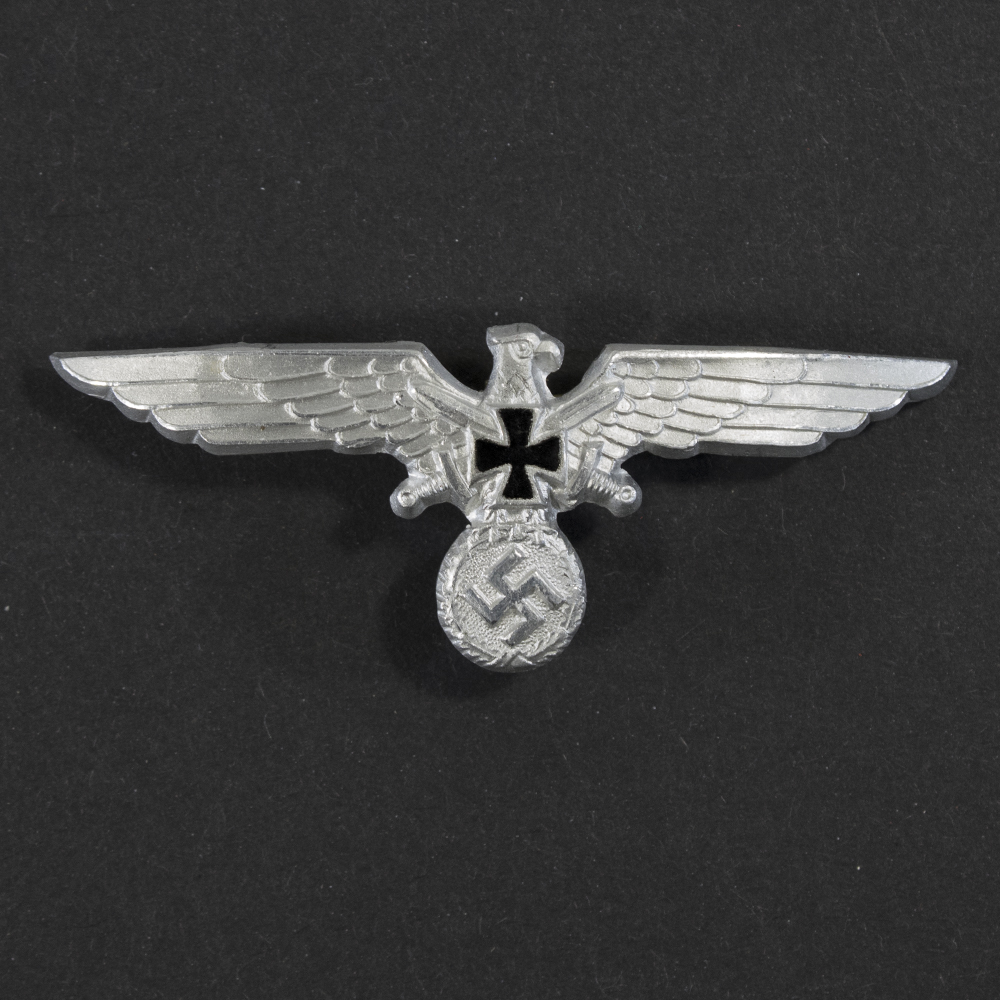 Front view of a WWII Kyffhäuserbund metal cap eagle, showing the spread‑winged eagle above the Kyffhäuserbund tower emblem. The raised metal details, contours, and overall finish of the badge are clearly visible.