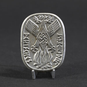 Overview photo of a WWII German “Deutsches Jugendfest 1935” tinnie, showing the full badge with its raised relief design, event inscription, and metal finish. The overall shape, imagery, and condition of the piece are clearly visible.