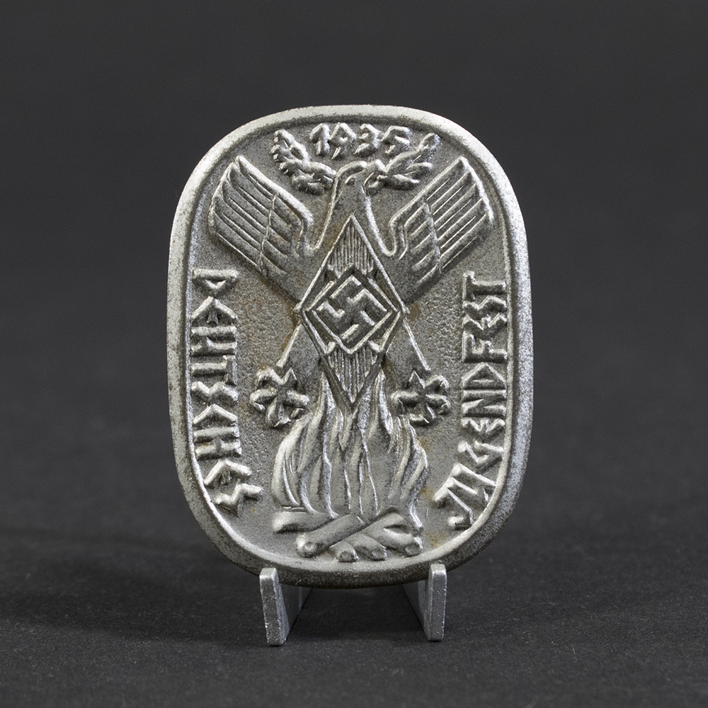 Overview photo of a WWII German “Deutsches Jugendfest 1935” tinnie, showing the full badge with its raised relief design, event inscription, and metal finish. The overall shape, imagery, and condition of the piece are clearly visible.