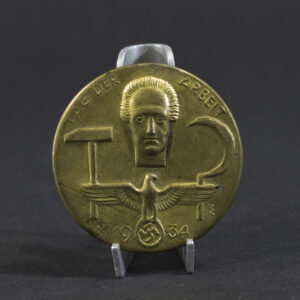 Overview photo of a WWII German “Tag der Arbeit 1934” tinnie, showing the full badge with its raised relief design, event inscription, and metal finish. The overall shape, imagery, and condition of the piece are clearly visible.