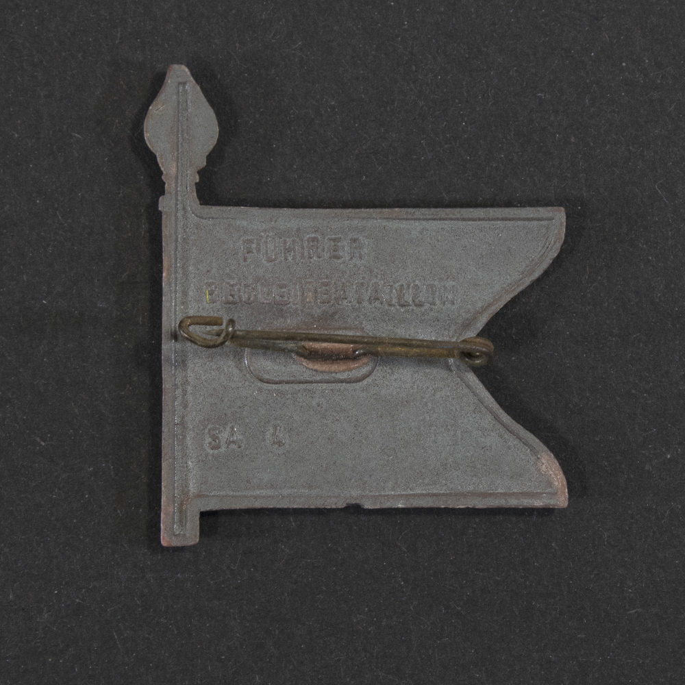 Close‑up of the back side of the same plastic miniature flag. A horizontal metal pin is attached to the rear, which is otherwise flat and unpainted. Small casting marks and subtle production details are visible in the plastic, along with the attachment points of the pin.