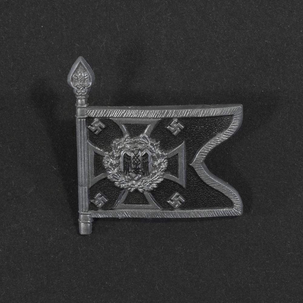 Close‑up of the front side of a small plastic Winterhilfswerk miniature flag associated with the Pioniere Mot. The rectangular flag shows an eagle emblem and raised lettering molded into the plastic. The surface has a glossy finish, and the relief details and edges are clearly visible despite minor wear.