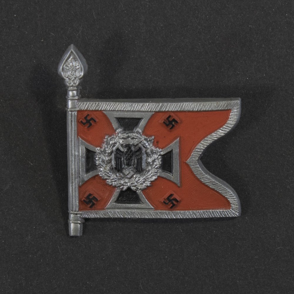 Close‑up of the front side of a small plastic Winterhilfswerk miniature flag associated with the Artillerie. The rectangular flag shows an eagle emblem and raised lettering molded into the plastic. The surface has a glossy finish, and the relief details and edges are clearly visible despite minor wear.