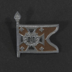Close‑up of the front side of a small plastic Winterhilfswerk miniature flag associated with the Aufklärungsabteilung . The rectangular flag shows an eagle emblem and raised lettering molded into the plastic. The surface has a glossy finish, and the relief details and edges are clearly visible despite minor wear.