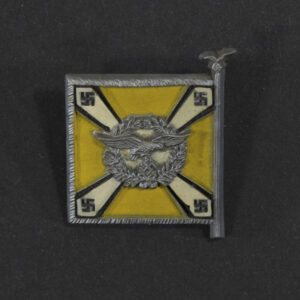 Close‑up of the front side of a small plastic Winterhilfswerk miniature flag associated with the Fliegertruppen. The rectangular flag shows an eagle emblem and raised lettering molded into the plastic. The surface has a glossy finish, and the relief details and edges are clearly visible despite minor wear.
