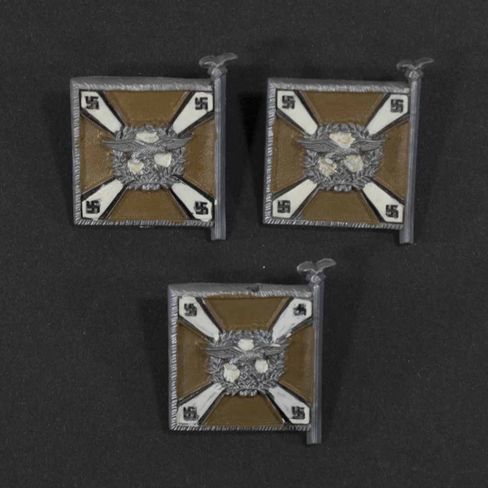 Close‑up of the front side of a small plastic Winterhilfswerk miniature flag associated with the Luftnachtrichtentruppe. The rectangular flag shows an eagle emblem and raised lettering molded into the plastic. The surface has a glossy finish, and the relief details and edges are clearly visible despite minor wear.