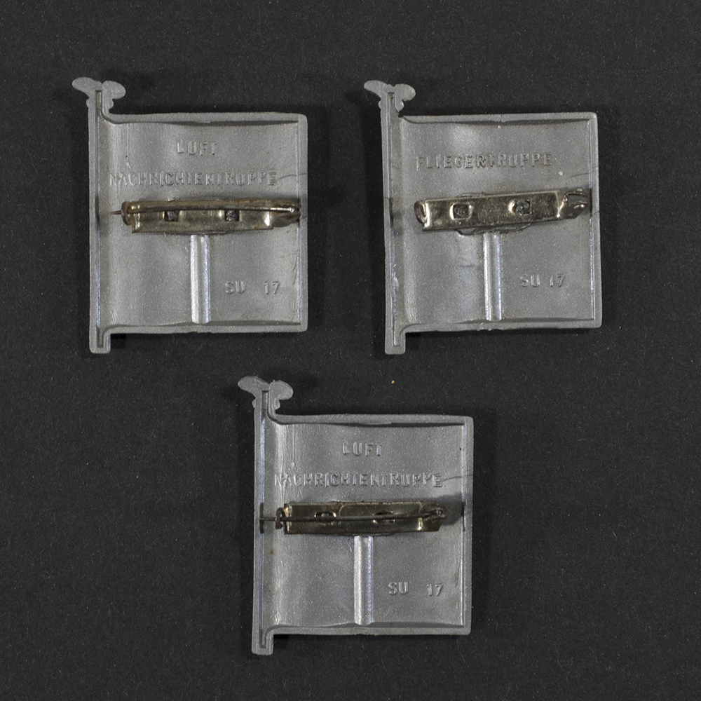 Close‑up of the back side of the same plastic miniature flag. A horizontal metal pin is attached to the rear, which is otherwise flat and unpainted. Small casting marks and subtle production details are visible in the plastic, along with the attachment points of the pin.