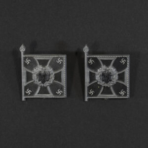 Close‑up of the front side of a small plastic Winterhilfswerk miniature flag associated with the Pioniere. The rectangular flag shows an eagle emblem and raised lettering molded into the plastic. The surface has a glossy finish, and the relief details and edges are clearly visible despite minor wear.
