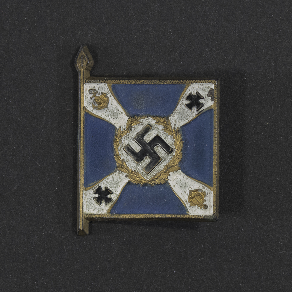 Close‑up of the front side of a small plastic Winterhilfswerk miniature flag associated with the Kriegsmarine Marineteile. The rectangular flag shows an eagle emblem and raised lettering molded into the plastic. The surface has a glossy finish, and the relief details and edges are clearly visible despite minor wear.