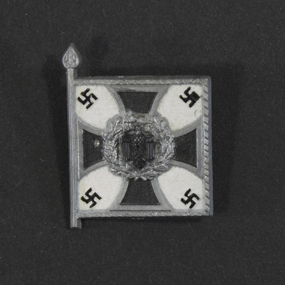 Close‑up of the front side of a small plastic Winterhilfswerk miniature flag associated with the Infanterie. The rectangular flag shows an eagle emblem and raised lettering molded into the plastic. The surface has a glossy finish, and the relief details and edges are clearly visible despite minor wear.