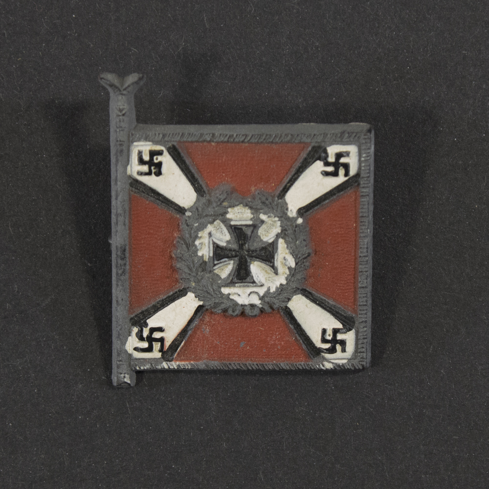 Close‑up of the front side of a small plastic Winterhilfswerk miniature flag associated with the Flakartillerie. The rectangular flag shows an eagle emblem and raised lettering molded into the plastic. The surface has a glossy finish, and the relief details and edges are clearly visible despite minor wear.