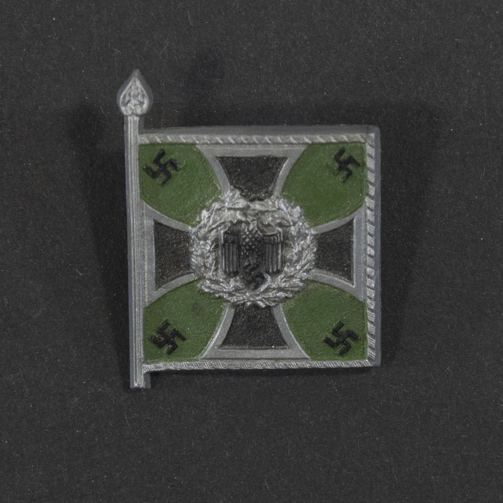 Close‑up of the front side of a small plastic Winterhilfswerk miniature flag associated with the Jäger. The rectangular flag shows an eagle emblem and raised lettering molded into the plastic. The surface has a glossy finish, and the relief details and edges are clearly visible despite minor wear.