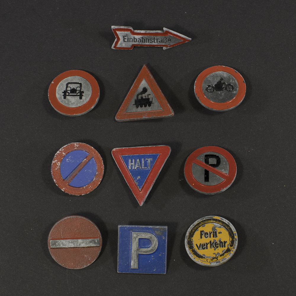 Front view of a complete set of ten German WWII Winterhilfswerk Verkehrszeichen badges made of zinc, showing different stylized traffic sign designs arranged together
