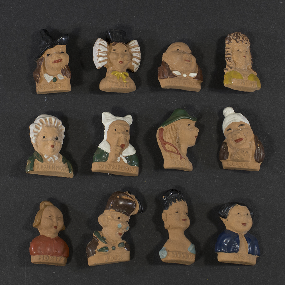 Front view of a complete set of twelve German WWII Winterhilfswerk Wilhelm Busch figurines, small painted figures based on characters from Wilhelm Busch stories, arranged together as a matching series.