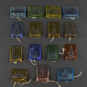 Front view of a complete set of sixteen German WWII Winterhilfswerk “Deutsche Baudenmäler” glass badges, each depicting a different famous German landmark or historic building, arranged together as a matched series.
