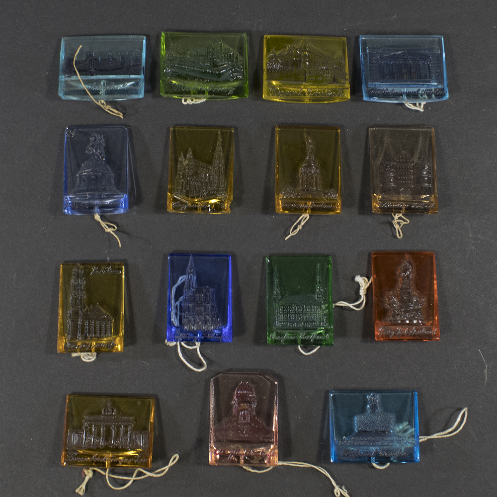 Front view of a complete set of sixteen German WWII Winterhilfswerk “Deutsche Baudenmäler” glass badges, each depicting a different famous German landmark or historic building, arranged together as a matched series.