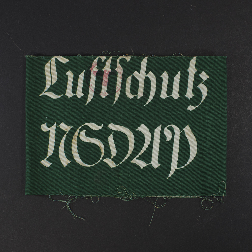 “Overview of a green WWII-era German Luftschutz armband made of cloth, showing printed lettering and the full band laid flat