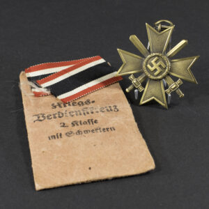 Overview of a World War II-era German War Merit Cross 2nd Class medal set displayed with its original paper issue bag, showing the bronze cross and accompanying packaging on a neutral background.