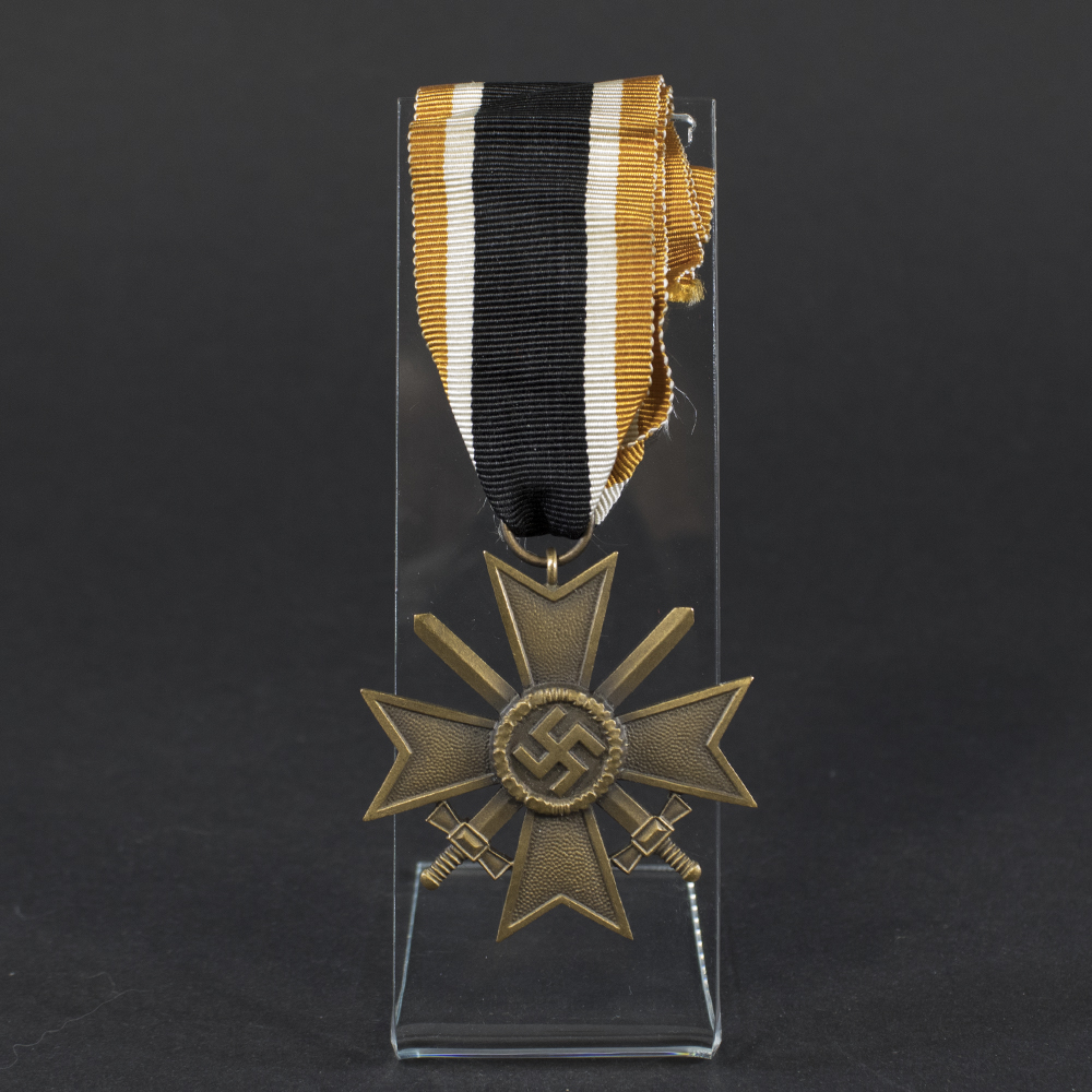 Overview of a World War II-era German War Merit Cross with swords, shown with its original ribbon, displaying the bronze cross suspended from a striped ribbon against a neutral background.