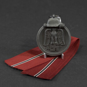 Overview of a World War II-era German Eastern Front Medal (Ostmedaille), shown with its ribbon, displaying the round medal suspended from a red, white, and black striped ribbon against a neutral background.
