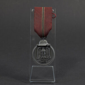 Overview of a World War II-era German Eastern Front Medal (Ostmedaille), shown with its ribbon, displaying the round medal suspended from a red, white, and black striped ribbon against a neutral background.