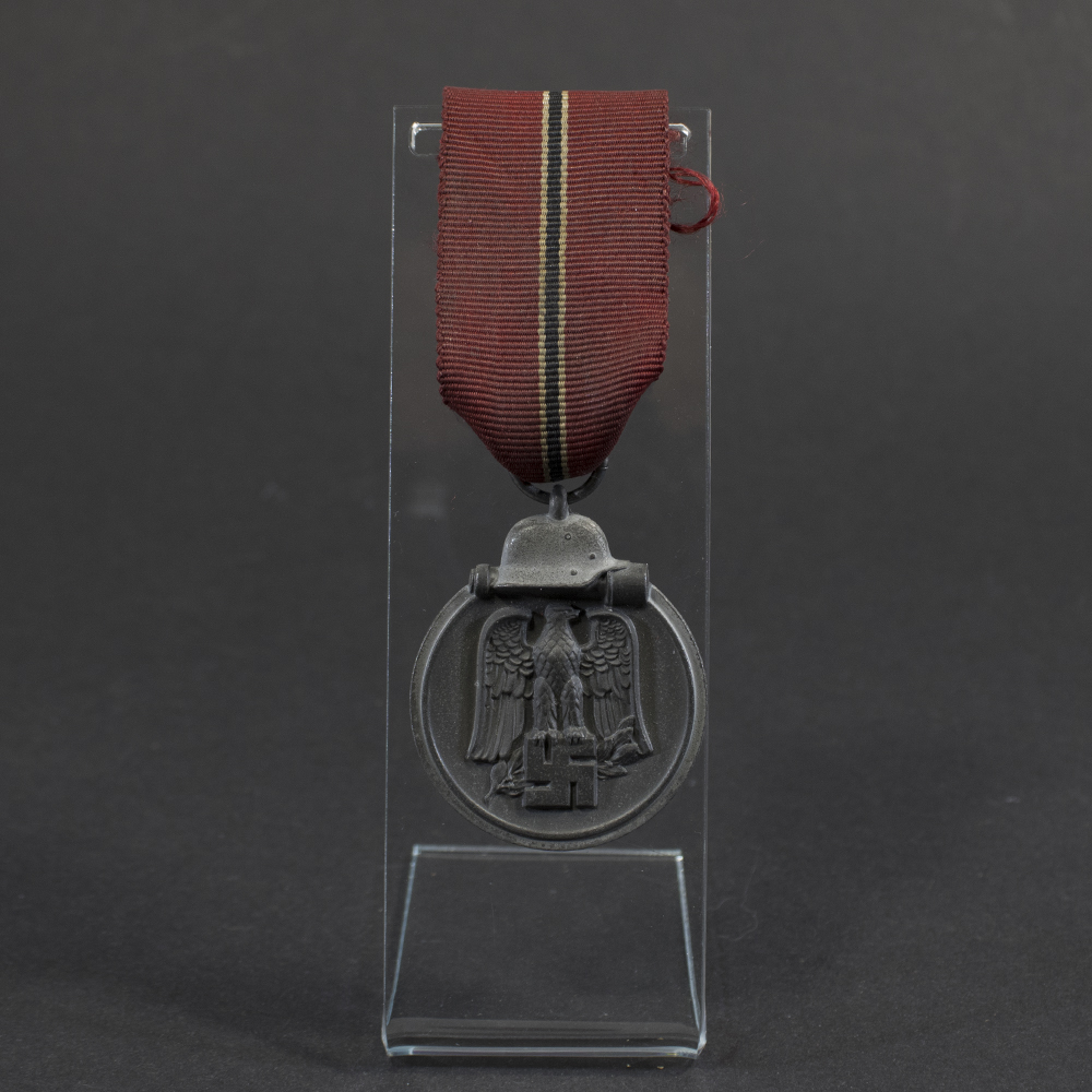 Overview of a World War II-era German Eastern Front Medal (Ostmedaille), shown with its ribbon, displaying the round medal suspended from a red, white, and black striped ribbon against a neutral background.