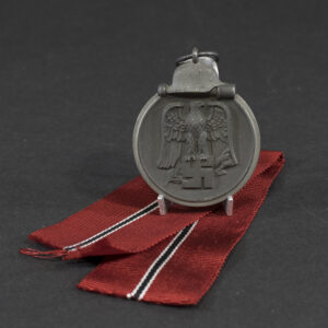 Overview of a World War II-era German Eastern Front Medal (Ostmedaille), shown with its ribbon, displaying the round medal suspended from a red, white, and black striped ribbon against a neutral background.