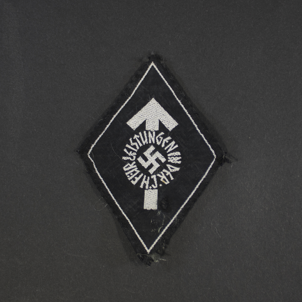 Full view of a WWII German Hitler Youth Proficiency Badge in cloth, silver grade. The diamond-shaped embroidered badge features a silver-colored border surrounding the distinctive Hitler Youth emblem on a dark fabric backing. The cloth shows light age-related wear and period-correct texture.