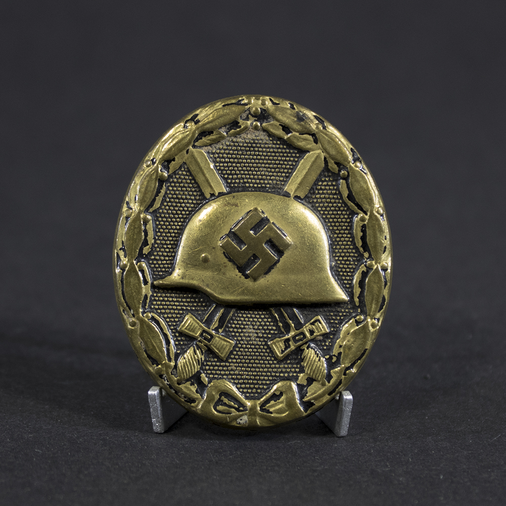Full view of a WWII German Black Wound Badge. The oval-shaped badge features a military helmet over crossed swords within a laurel wreath. Most of the original black finish has worn away, exposing the underlying metal and creating a heavily aged appearance with visible wear and patina.