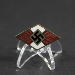 Full view of a WWII German Hitler Youth cap badge. The metal badge features the distinctive Hitler Youth diamond emblem and shows age-related wear and patina. The reverse is maker-marked “M/13,” identifying the manufacturer as Christian Lauer.
