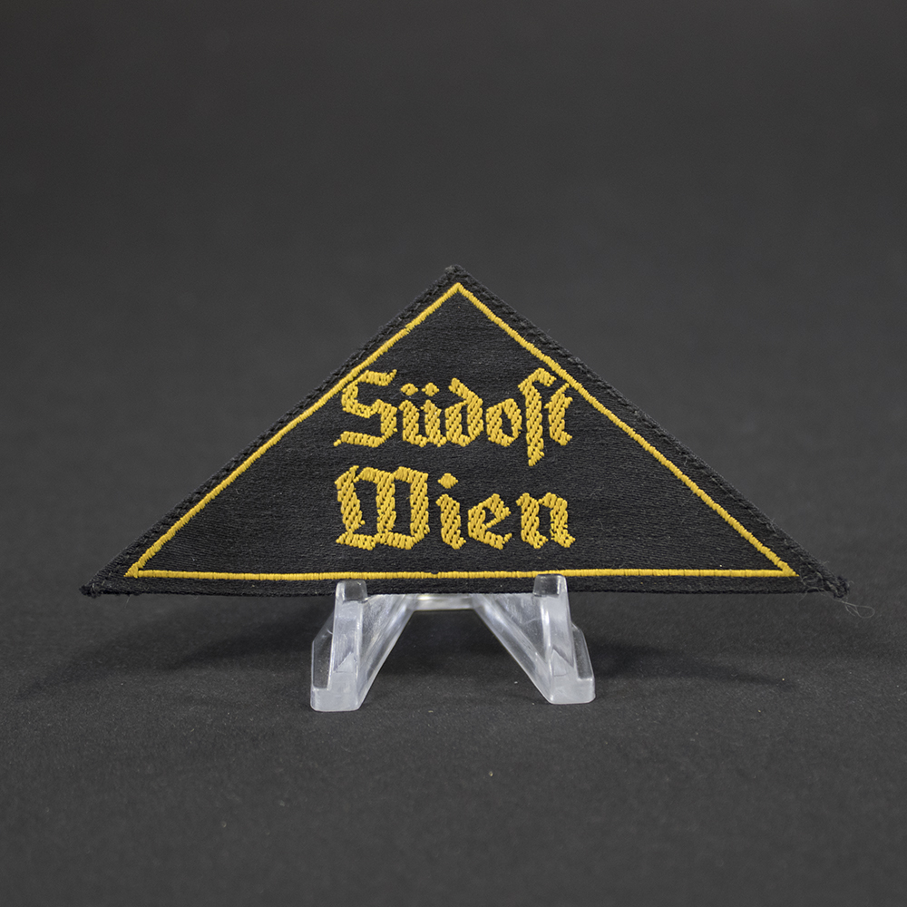 Overview of a Hitler Youth (HJ) “Gebietsdreieck Südost Wien” cloth insignia, triangular in shape with embroidered lettering, shown in full view to display its overall condition, color, and construction.