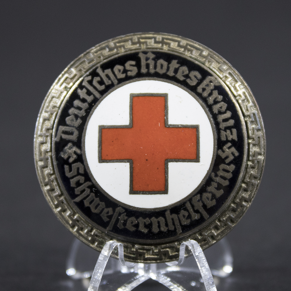 Close-up of the front of the DRK Schwesternhelferin brooch, highlighting the central emblem, enamel or metal finish, lettering, and fine details of the badge design.