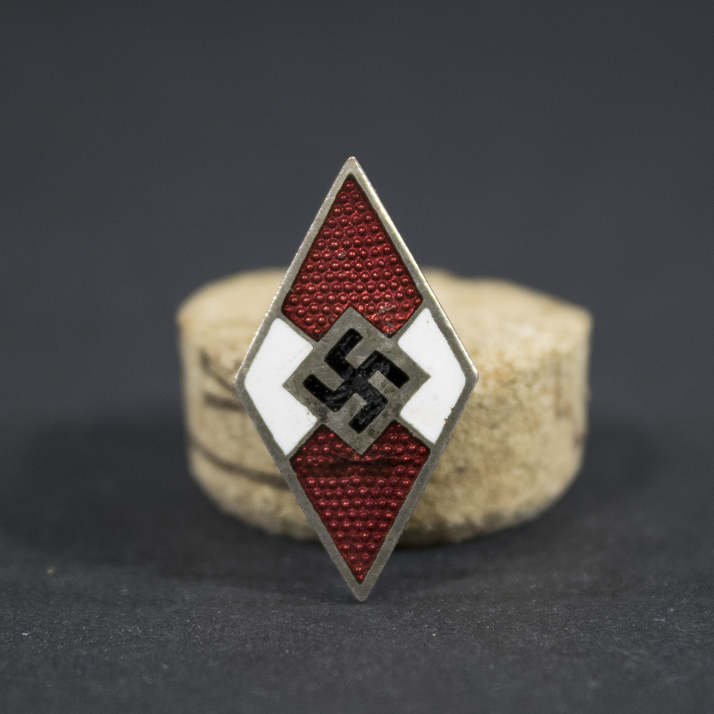 Overview of an M1/34-marked Hitler Youth membership pin, displayed in full view to show the diamond-shaped badge, enamel finish, attachment hardware, and overall condition.