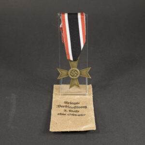 Overall view of a War Merit Cross, 2nd Class, suspended from its ribbon. The bronze-colored cross features a central wreath with swastika emblem and lacks the crossed swords found on the combat award version.