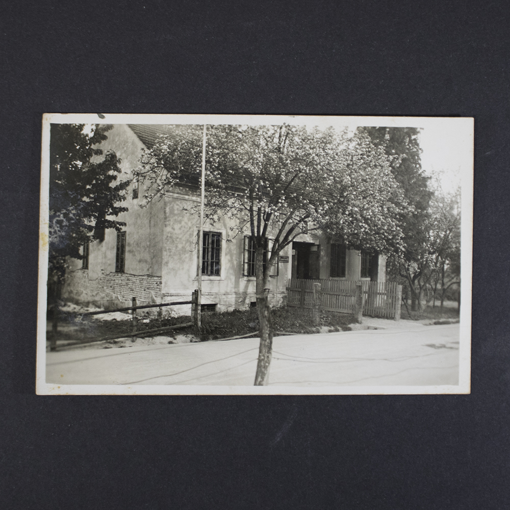 Black-and-white historical postcard depicting a residential house in Leonding, Austria. The building is shown from the street, surrounded by trees and a wooden fence. The photograph captures the exterior of the house identified as the parents' home in Leonding, with a tree positioned in the foreground.