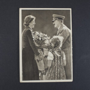 Black-and-white German postcard titled “Deutscher Frühling,” showing Adolf Hitler receiving a bouquet of flowers from a young woman while two children stand nearby. The photograph, taken by Heinrich Hoffmann, captures a formal public presentation scene and is printed in a white-bordered postcard format.