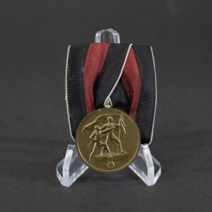 WWII German Sudetenland Medal mounted on a parade-style medal bar with folded black, red, and white ribbon. The bronze medal features two standing figures before a flag, with an eagle and swastika emblem at the bottom of the design.