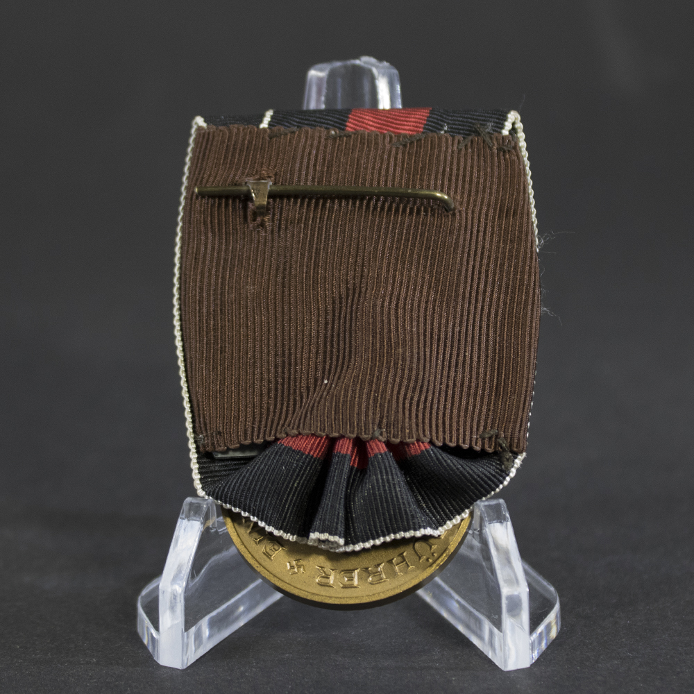 Reverse side of a WWII German Sudetenland Medal bar showing the original brown cloth backing and horizontal pin fastening system. Part of the bronze medal is visible beneath the folded ribbon, with period stitching and mounting details intact.
