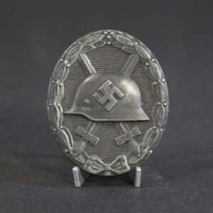 WWII German Silver Wound Badge (Verwundetenabzeichen in Silber) displayed upright on a stand. The oval badge features a steel combat helmet with a swastika emblem over crossed swords, surrounded by a laurel wreath with a bow at the base. Silver finish with visible period wear and patina.
