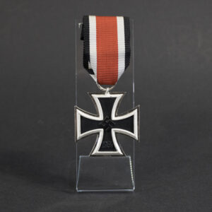 Close-up front view of a German Iron Cross 2nd Class (Eisernes Kreuz 2. Klasse) 1939 medal. The cross has a black center with a silver-colored border and features a raised swastika at the center. The year “1939” is visible on the lower arm. The medal is suspended from a metal ring and displayed on a clear acrylic stand against a dark background.