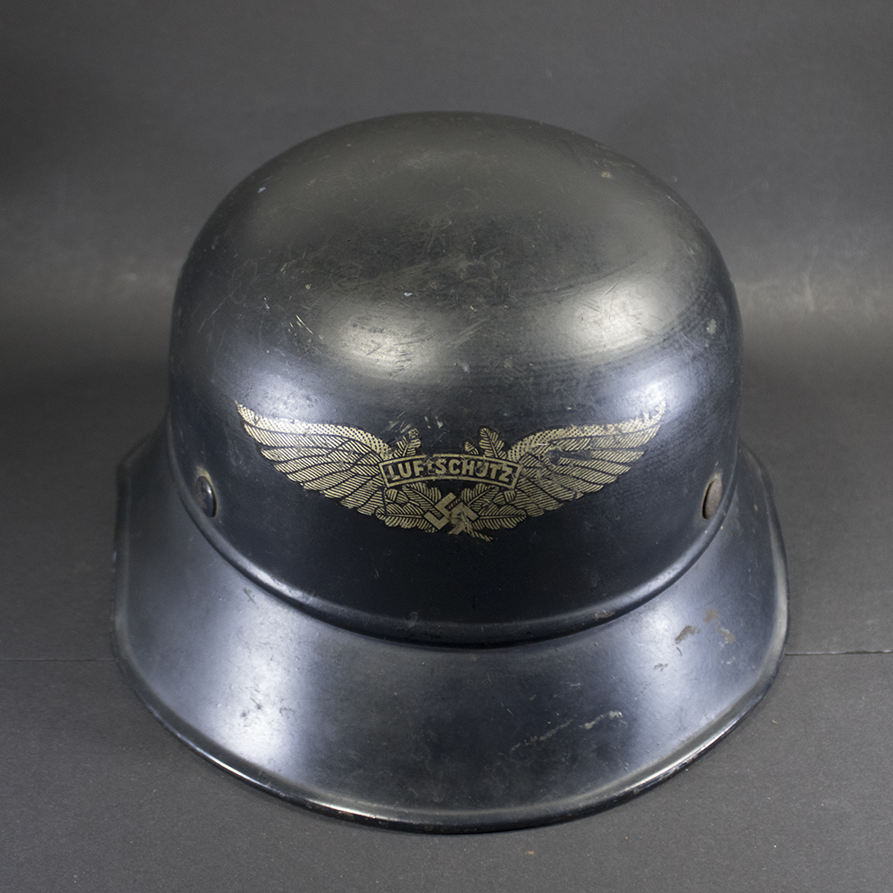 Front view from an elevated angle of a dark blue-grey WW2 German Luftschutz gladiator helmet featuring a gold decal.