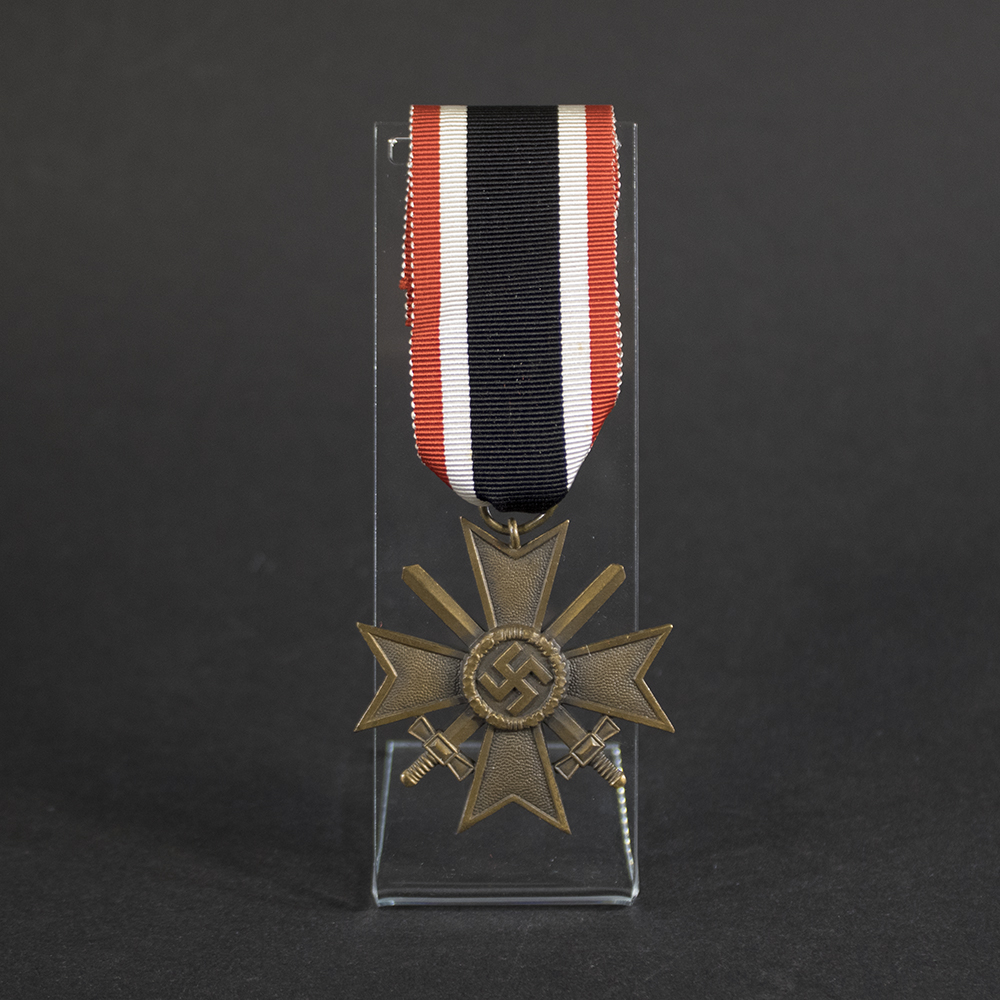 Front view of a WW2 German War Merit Cross 2nd Class with Swords, featuring a pebbled bronze Maltese cross, crossed swords, and central swastika attached to its original red, white, and black ribbon on a clear display stand.