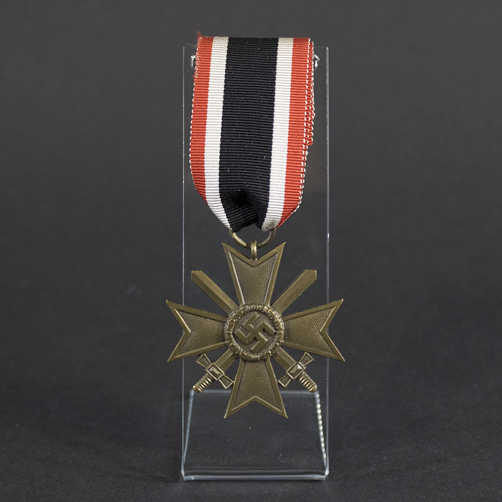 Front view of a WW2 German War Merit Cross 2nd Class with Swords, featuring a pebbled bronze Maltese cross, crossed swords, and central swastika attached to its original red, white, and black ribbon on a clear display stand.