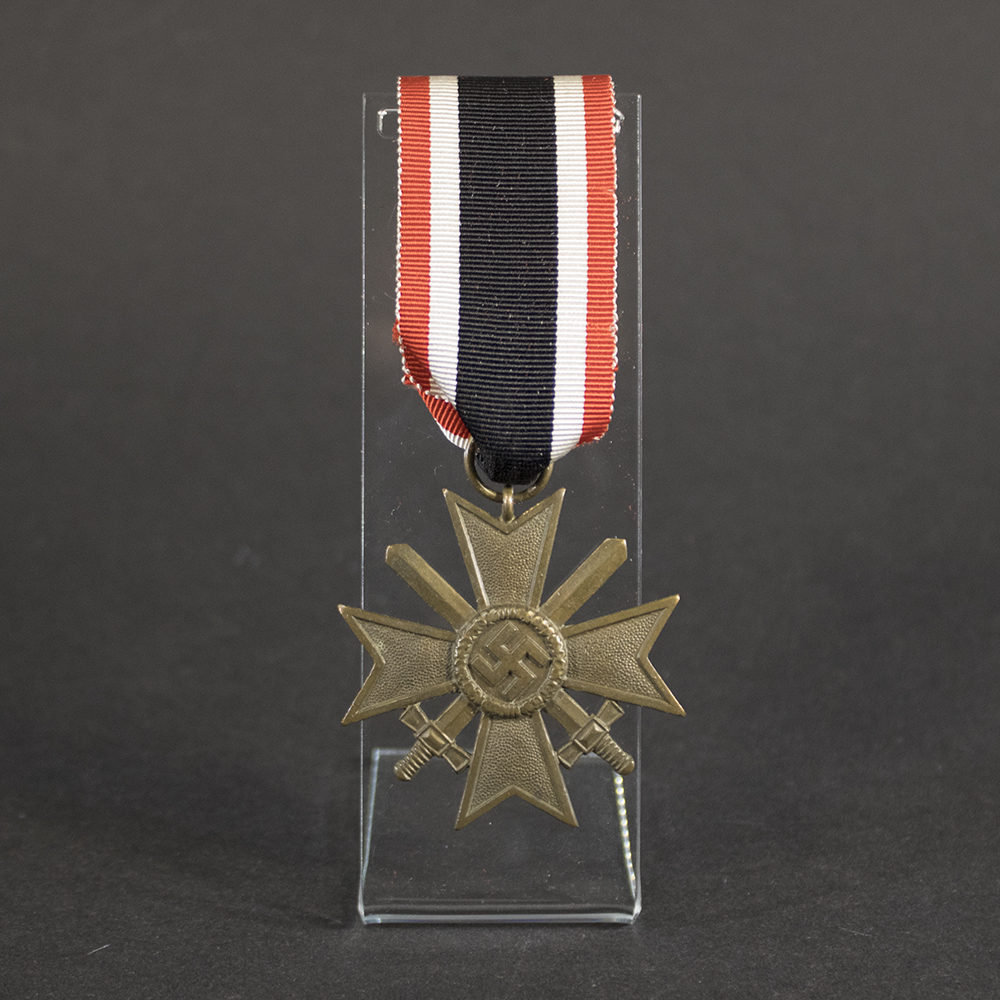 Front view of a WW2 German War Merit Cross 2nd Class with Swords, featuring a pebbled bronze Maltese cross, crossed swords, and central swastika attached to its original red, white, and black ribbon on a clear display stand.